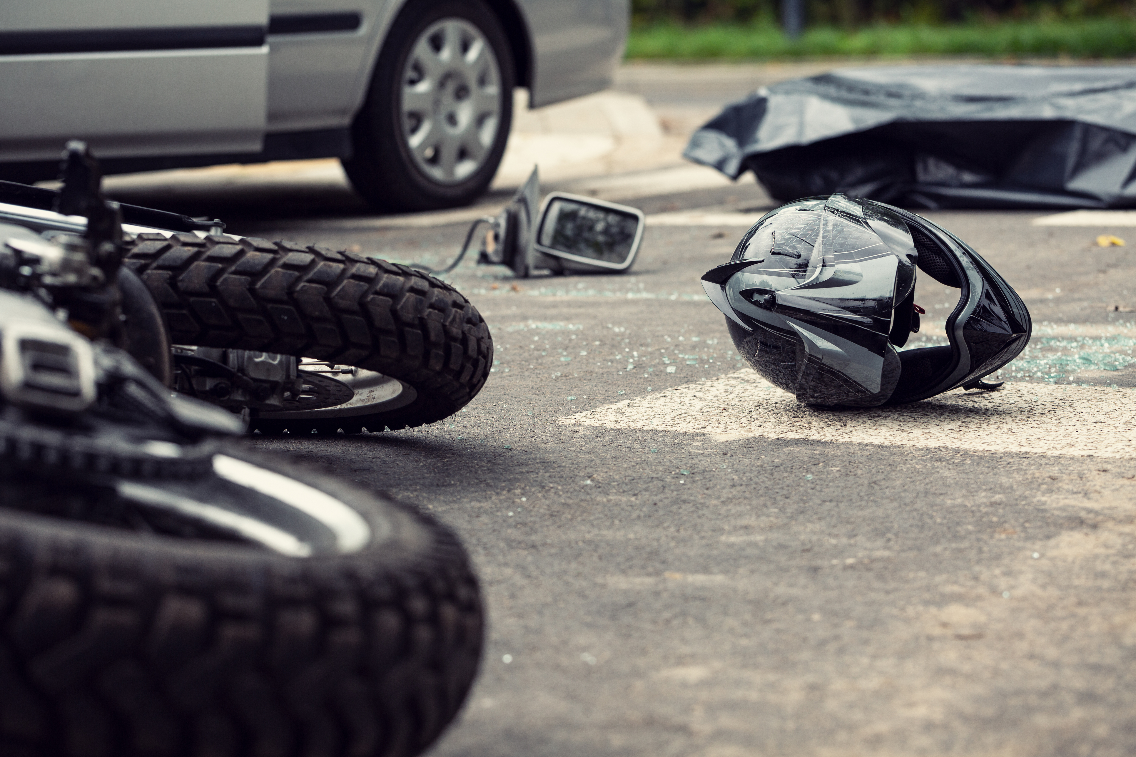 Motorcycle accident scene showing a fallen bike, damaged helmet, and debris on the road near a car