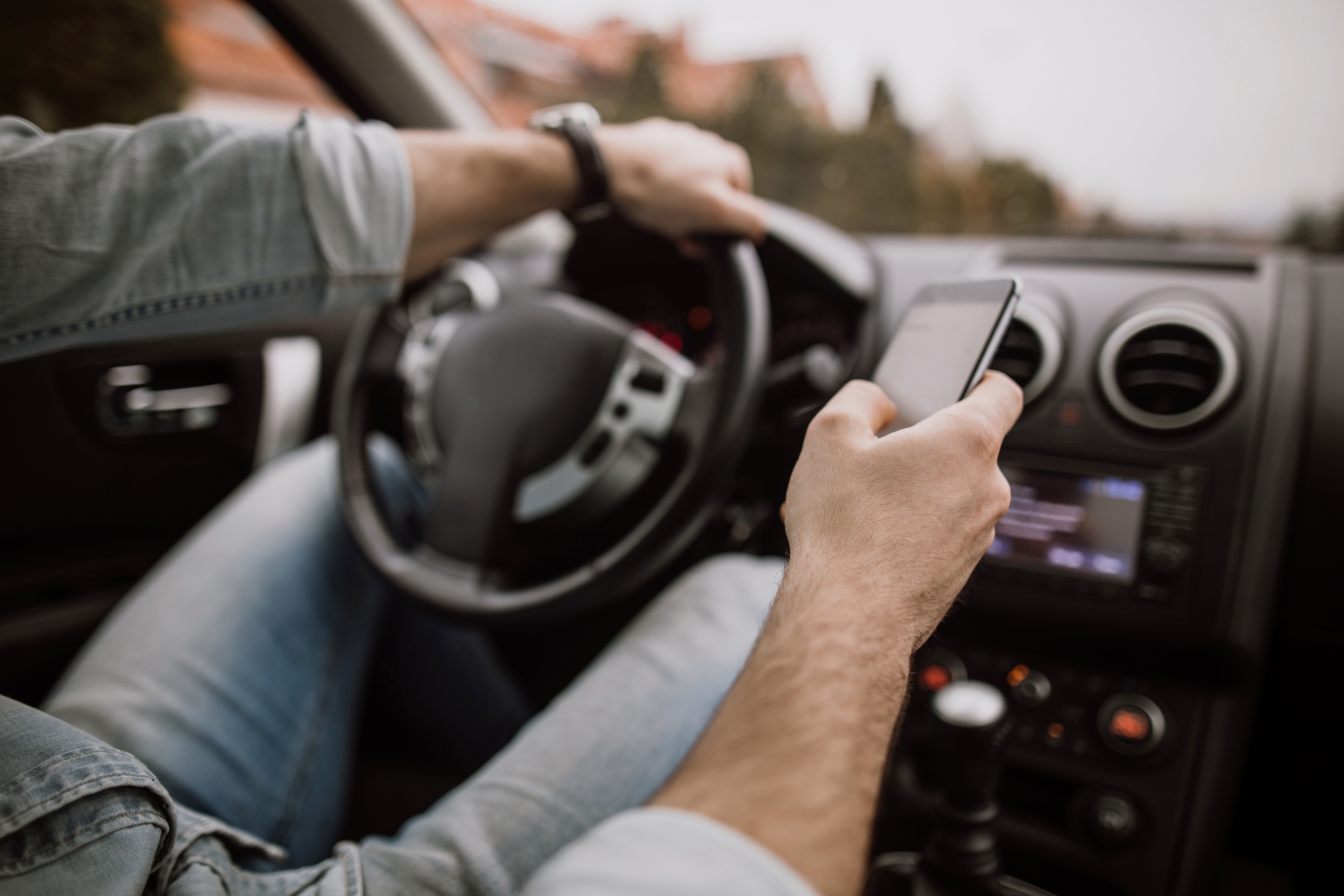 Driver using phone while driving behind a motorcycle, illustrating how distracted driving can cause motorcycle accidents 