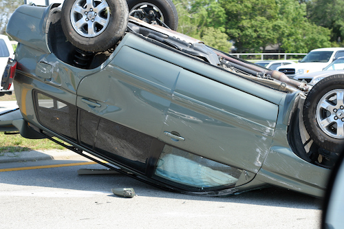 Overturned teal SUV with scratches on the side and the airbags deployed.