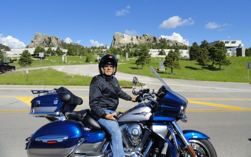 Man wearing a helmet sits on a blue motorcycle parked on the roadside under a clear sky, representing a real life motorcycle accident case featuring in a legal report.