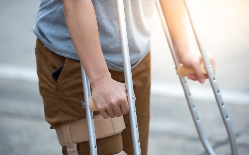 A person in a grey t-shirt and khaki pants leaning on crutches, deciding whether to hire a personal injury lawyer.