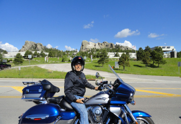 Man wearing a helmet sits on a blue motorcycle parked on the roadside under a clear sky, representing a real life motorcycle accident case featuring in a legal report.