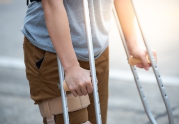 A person in a grey t-shirt and khaki pants leaning on crutches, deciding whether to hire a personal injury lawyer.